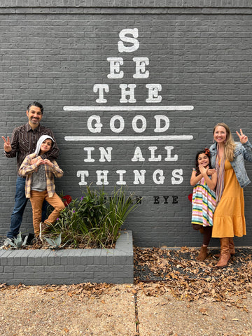Two adults and two children standing in front of a sign that says "See the good in all things"
