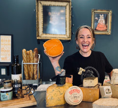 Cheesemonger Ivy at Second Mouse Cheese holding up a half wheel of mimolette