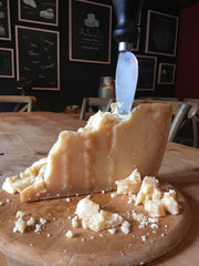 Wedge of Parmigiano-Reggiano with a parm knife sticking out of it.