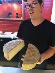 Cheesemonger holding two halves of a cut wheel of natural rinded raw milk cheese