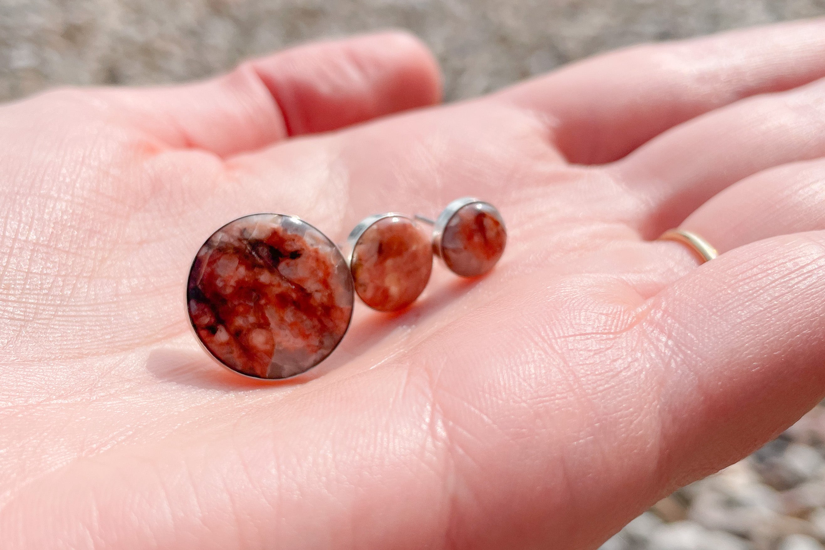 All three of Waystone's stud confluence earrings on a white hand comparing the different sizes