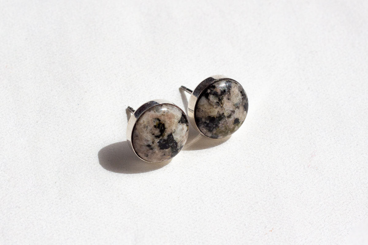 A pair of speckled stone confluence stud earrings from Waystone with a white background and a dark shadow