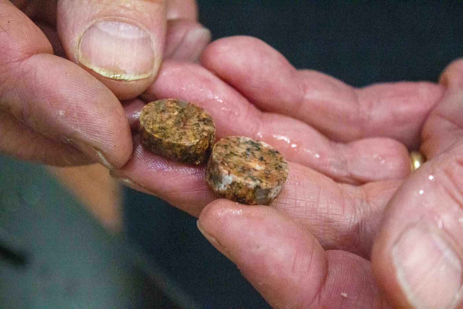 A man's hand holds cut cylindrical rounds of brown stone to turn into cufflinks