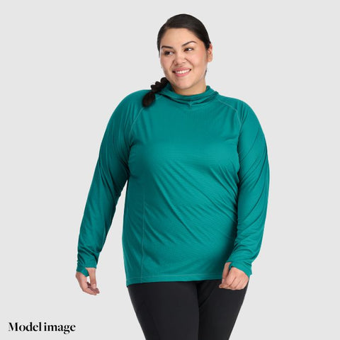 woman standing against grey background wearing a green long sleeved top