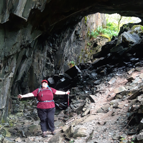fat woman stands arms outstretched near a rocky arch