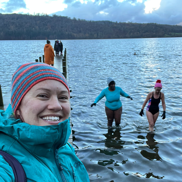 women wearh8infg a green coat and striped beanie hat with wild swimmers in the background