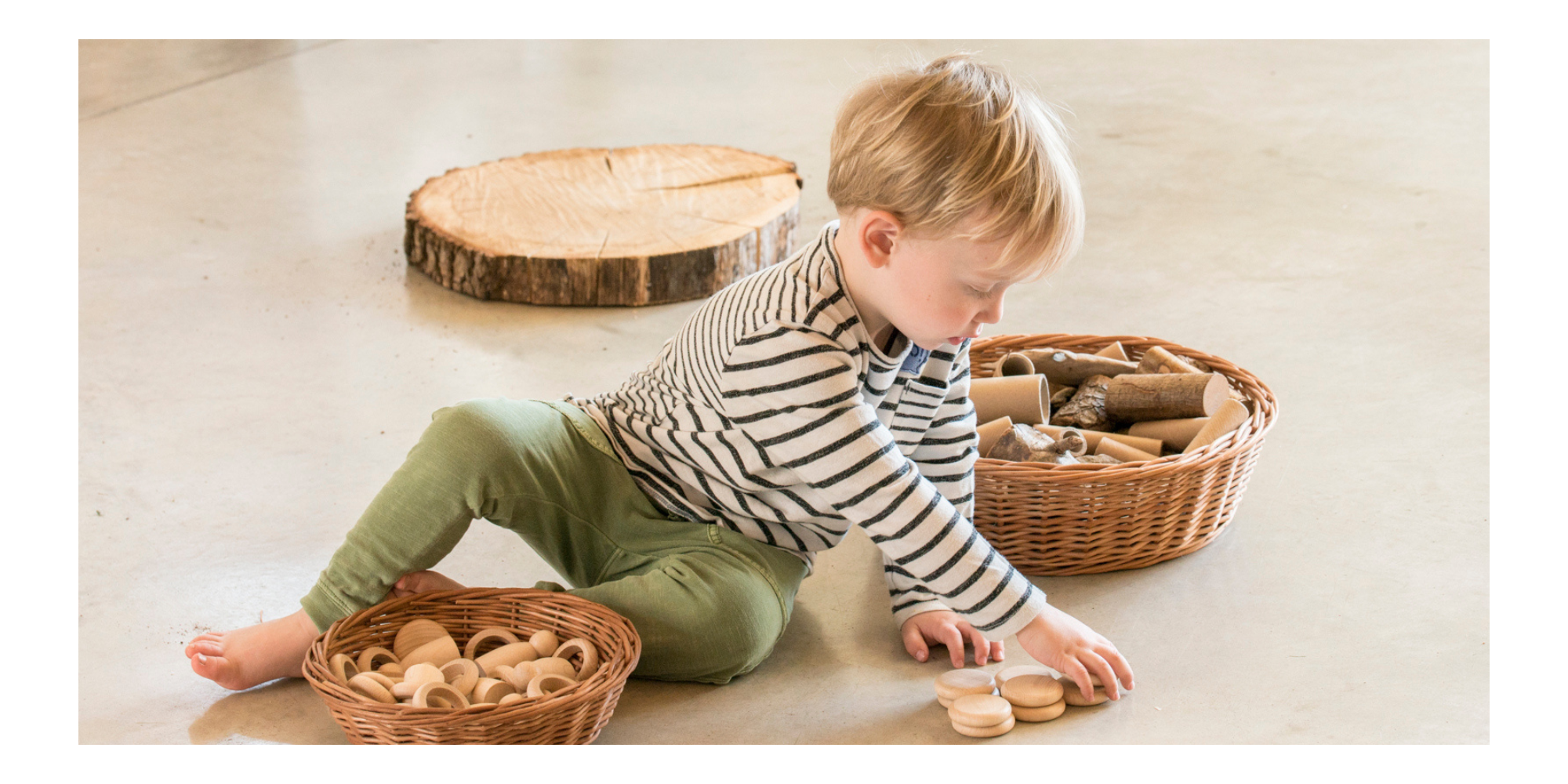 Kind sitzt am Boden und spielt mit Holzspielzeug von Grapat