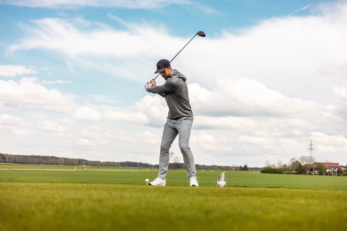 Harry Kane hits a tee shot with a driver on a golf course.