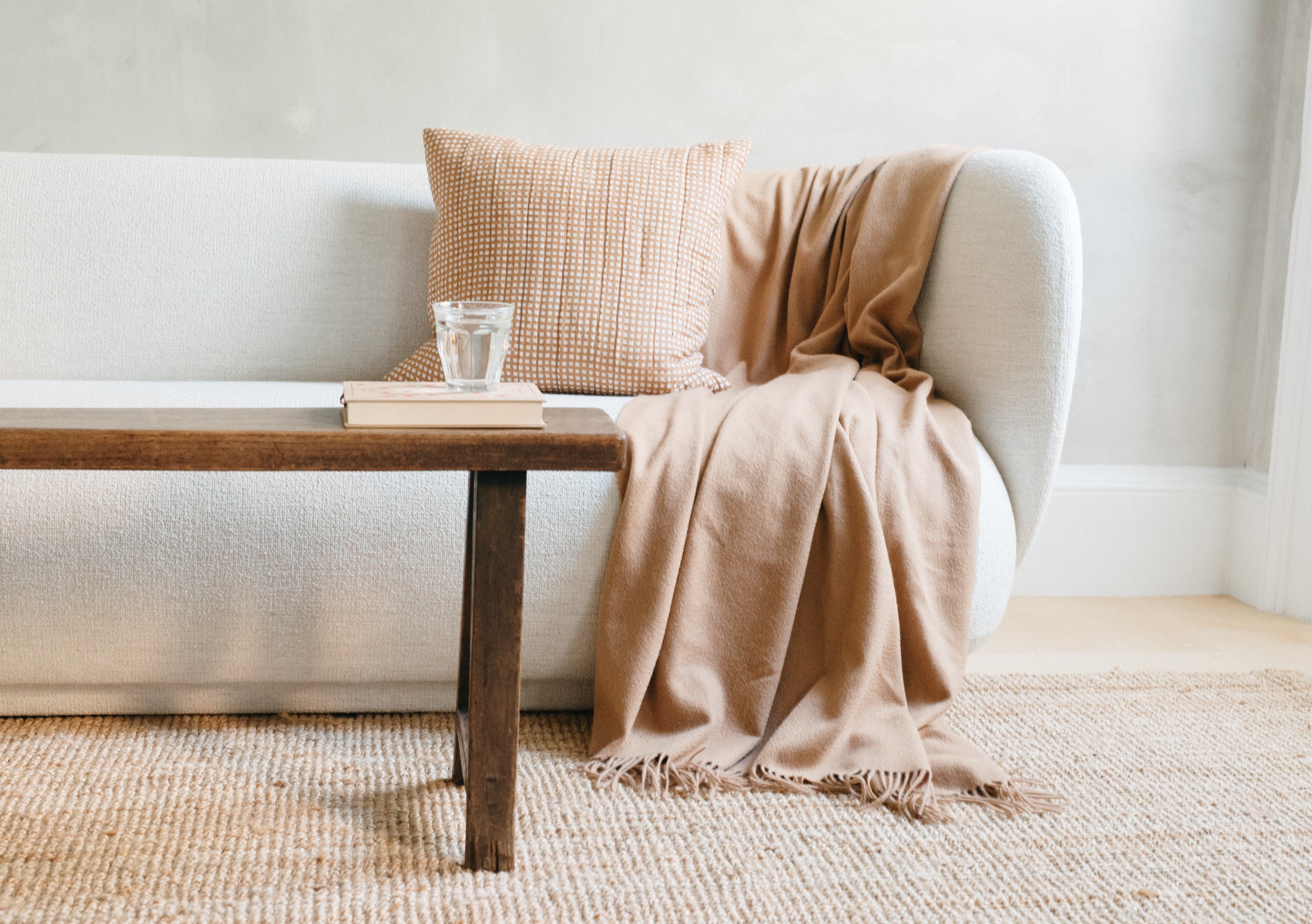 A camel lambswool blanket draped over the side of a white boucle textured couch