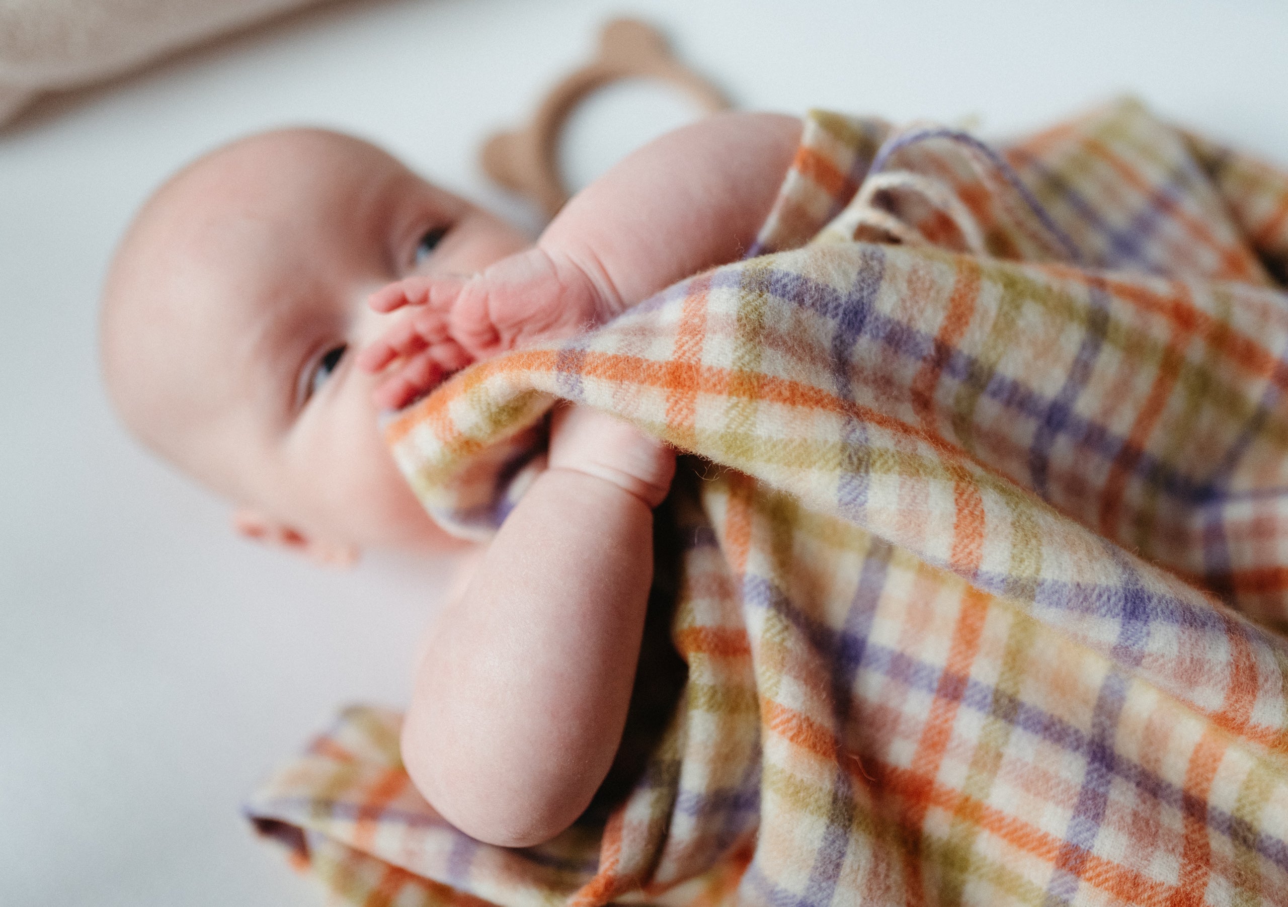 Close up of a baby lying in a crib with a colourful gingham baby blanket covering it