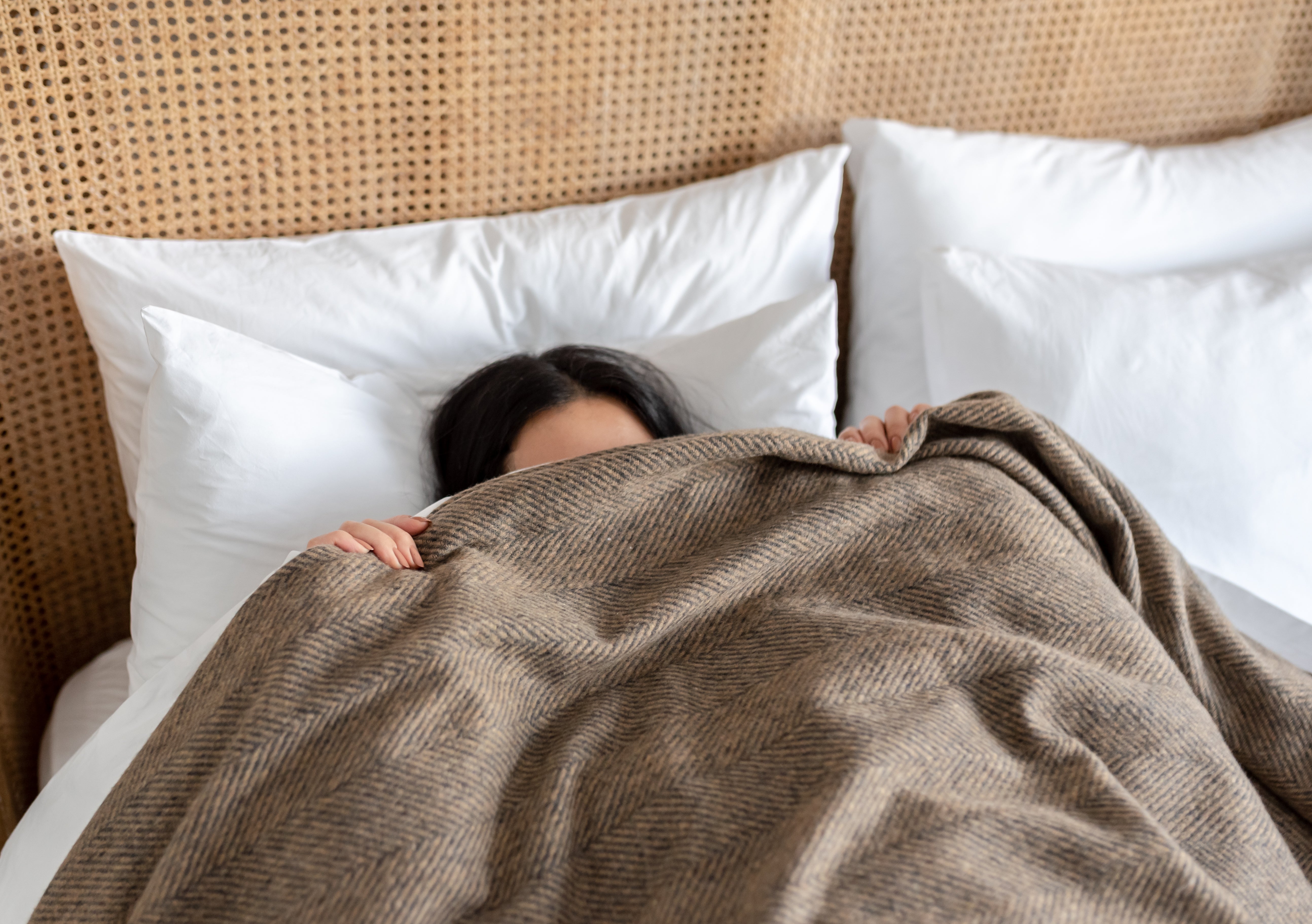 A girl lying in bed trying to sleep with a wool blanket pulled up across her face