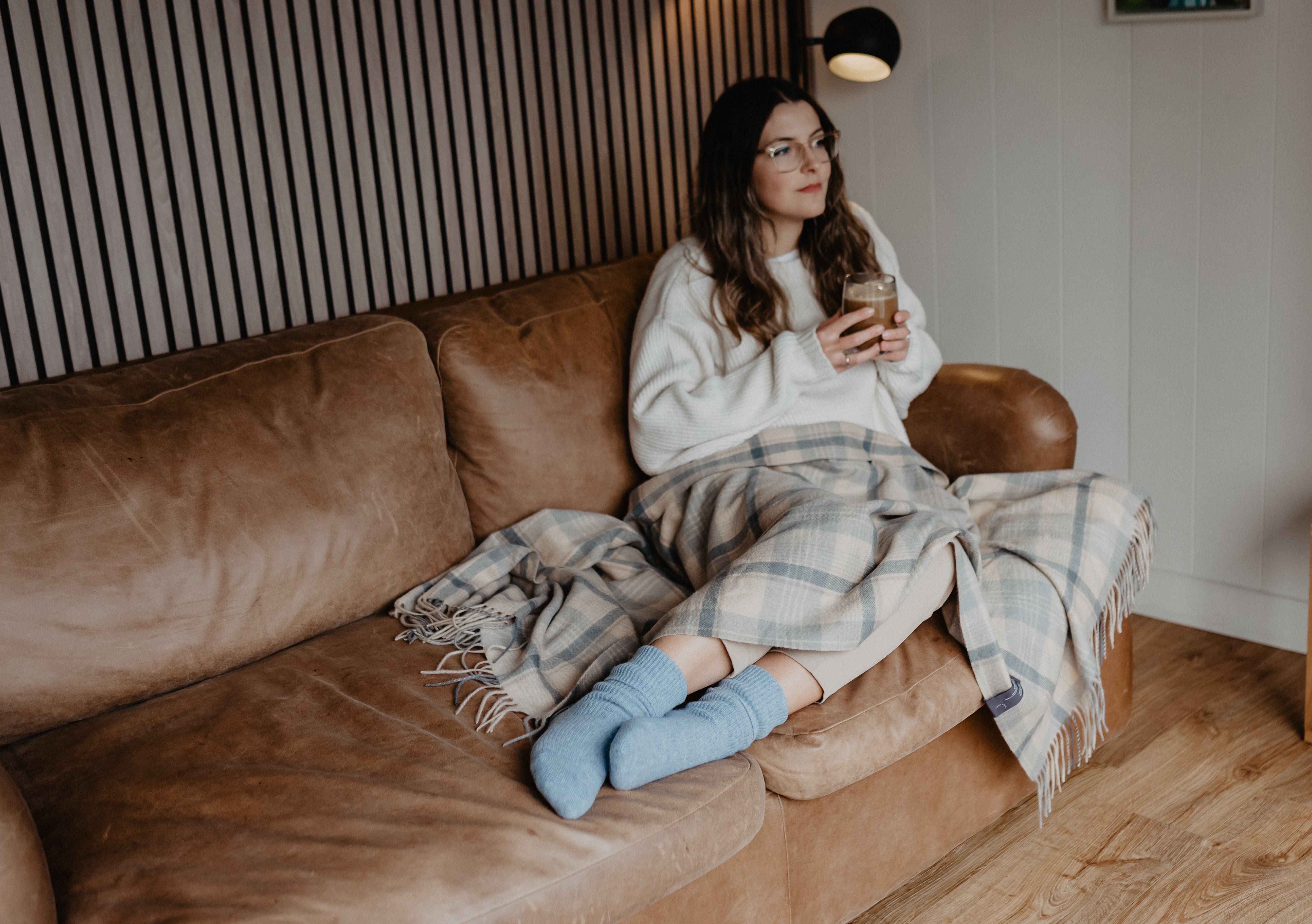 A girl sat on a couch with a knee blanket draped across her lap and wearing bed socks to help her sleep