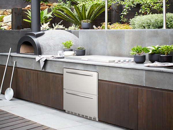  Side view of an outdoor kitchen setup featuring the 5.12 Cu Ft Outdoor Refrigerator with Drawer Design 160 cans installed under the kitchen table beside the pizza oven, and surrounded by other kitchen appliances