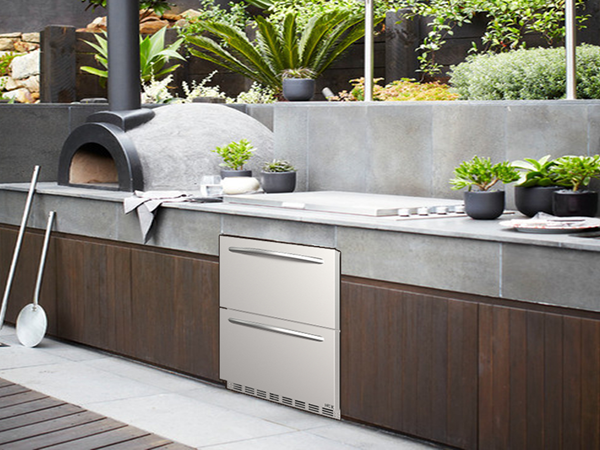  Side view of an outdoor kitchen setup featuring the 5.12 Cu Ft Undercounter Beverage Outdoor Refrigerator Drawer Design installed under the kitchen table beside the pizza oven, and surrounded by other kitchen appliances