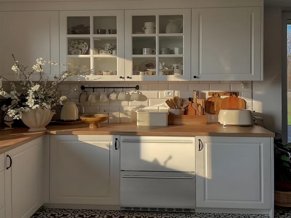  Side view of a retro-style kitchen setup with a white theme, featuring the 5.12 Cu Ft Outdoor Refrigerator with Drawer Design 160 cans installed under the kitchen table in the center. The refrigerator is surrounded by other kitchen appliances