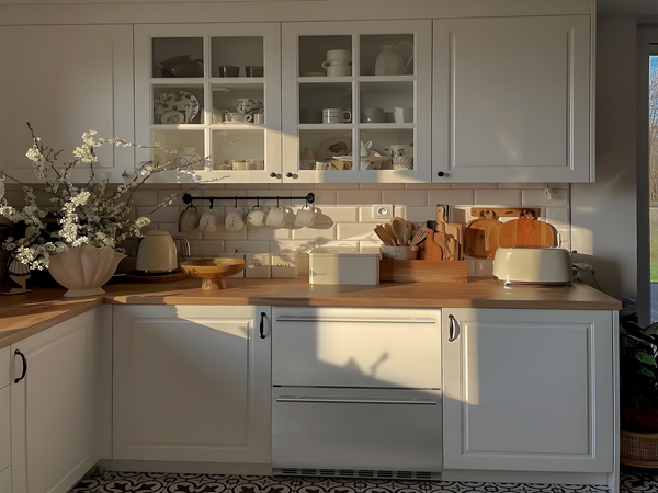  Side view of a retro-style kitchen setup with a white theme, featuring the 5.12 Cu Ft Undercounter Beverage Outdoor Refrigerator Drawer Design installed under the kitchen table in the center. The refrigerator is surrounded by other kitchen appliances