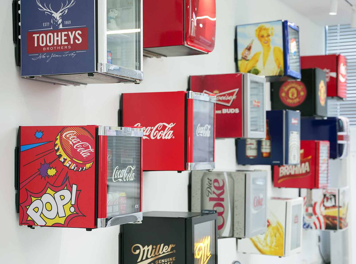 Display of beverage fridges adorned with iconic designs and brand names of globally renowned beverage giants like Coca-Cola, Miller, and Budweiser, showcasing the increasing reliability and prestige associated with these brands