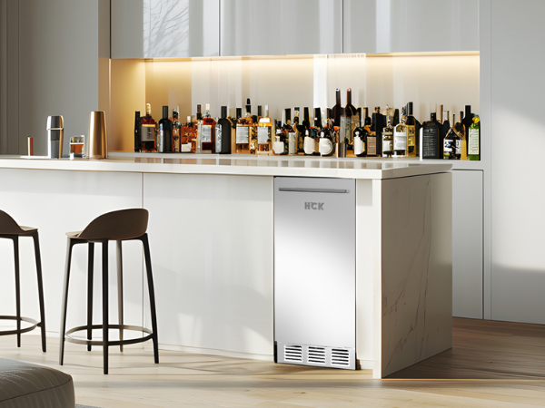 Side view of a kitchen setup with a 60 lbs Stainless Steel Outdoor Refrigerator Ice Maker positioned beneath the kitchen table in the right corner. In the background on the table are various bottles of wine