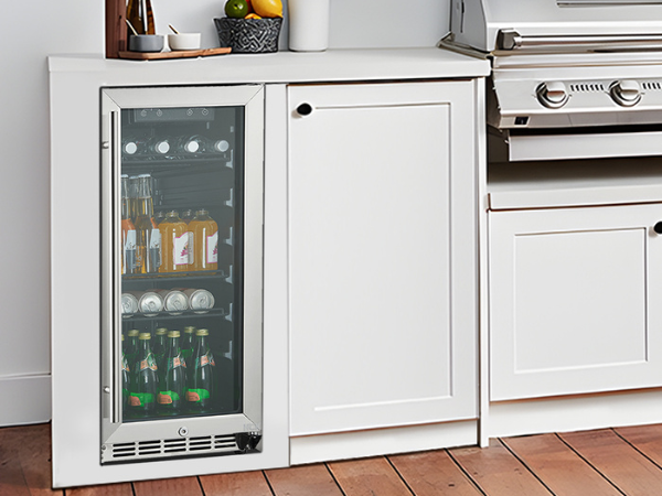 Side view of a modern kitchen setting with the 3.2 Cu Ft Compact Beverage Outdoor Refrigerator 96 cans installed under the kitchen counter, positioned next to a barbecue grill