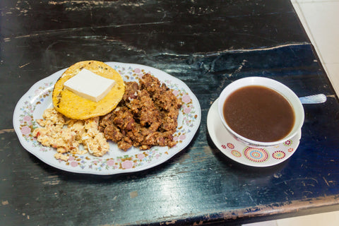 Arepa with cheese served with eggs along with a cup of hot chocolate
