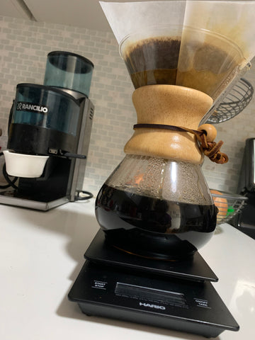 Chemex pitcher with filter on weight scale with coffee grinder in the background