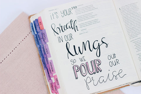 Open Bible with handwriting that says it's your breath in our lungs so we pour out our praise.