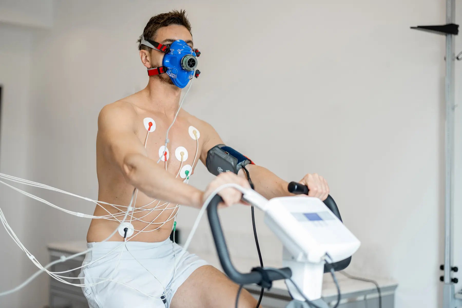 Modern VO2 testing with a man wearing a respiratory mask and sensors while cycling in a lab setting.