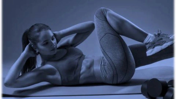 femme brune avec de longs cheveux tenus en catogan est allongée sur un tapis de gym et fait des abdominaux - image pour illustrer un article sur les bienfaits de la phycocyanine pour le sport et l'endurance