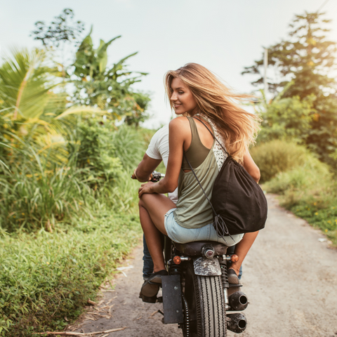 Smiling Women passenger on motorbike, looking back,  tropical background 