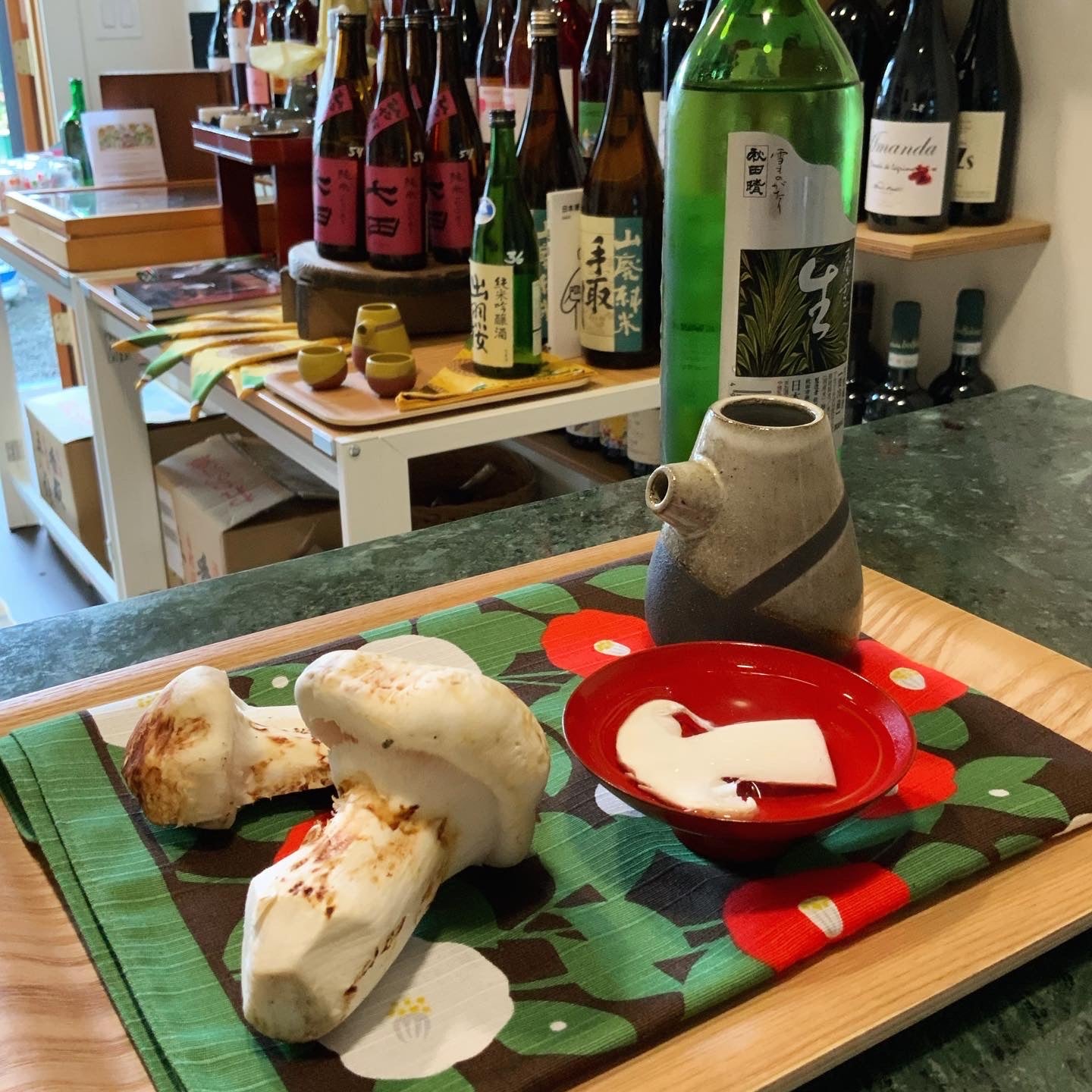 A wooden tray with a carafe of hot sake, two matsutake mushrooms, a bottle of sake and a shallow red hirahai.