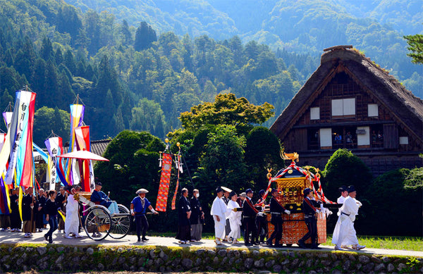 Doburoku Matsuri festival: a procession of people dressed in traditional garb and carrying flags walk through the UNESCO world heritage site with beautiful mountains in the background