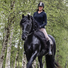 Ägaren till Natural Winner rider på sin frieserhäst med björkar i bakgrunden