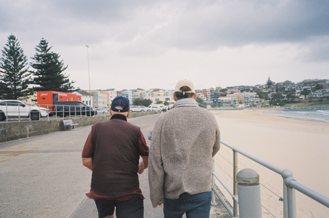 Two people walking down the sidewalk next to the sand at Bondi.