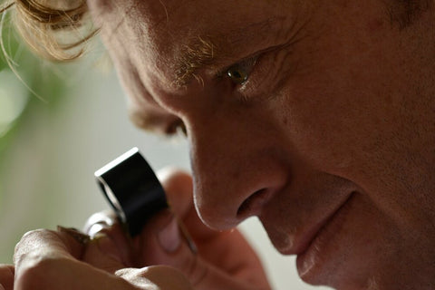 Nicky Burles holds jewellers loupe to face, examining an engagement ring