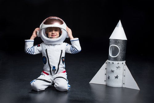 Kid in space suit next to a toy rocket