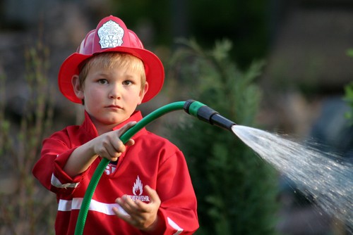 Boy in red fireman suit with spraying garden hose