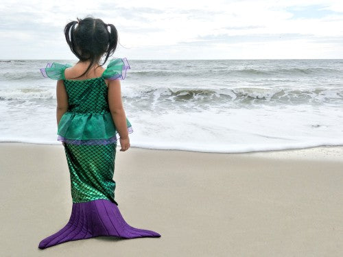 Little girl dressed as a mermaid contemplates the sea