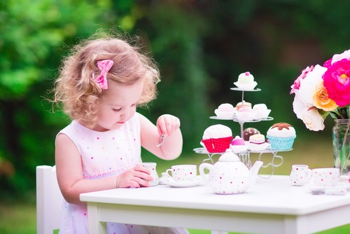 Little girl in backyard having a tea party with cakes