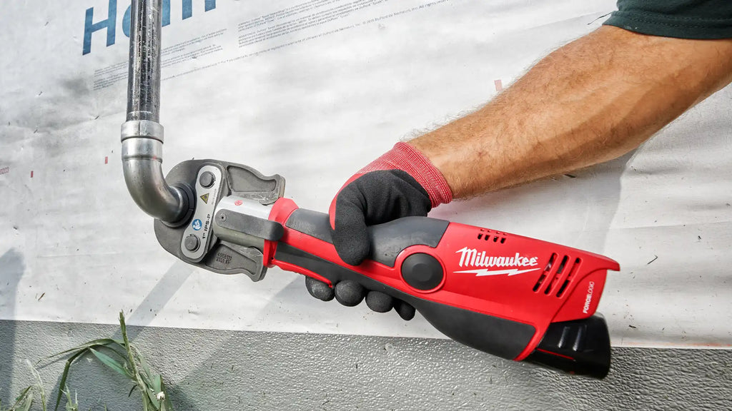Action shot of a professional using the Milwaukee M12 FORCE LOGIC Press Tool on a metal pipe, demonstrating the tool's practical application in a construction setting