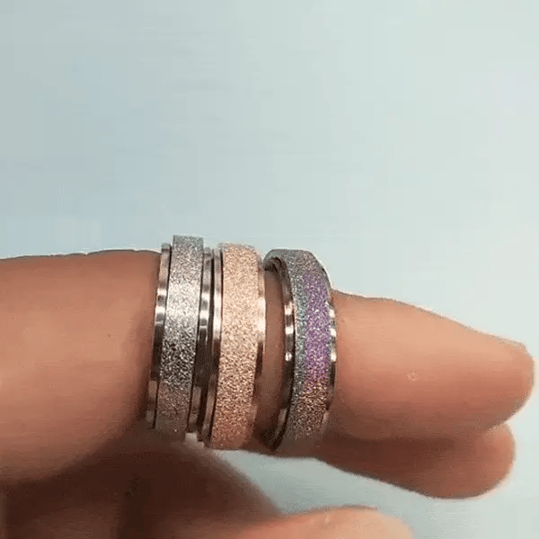 a finger with three spinner rings on it in different colours, silver, gold, and rainbow