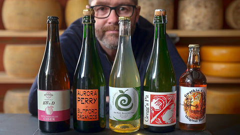 Chris of Cork and Crown in front of a wall of cheese and with a collection of artisan ciders