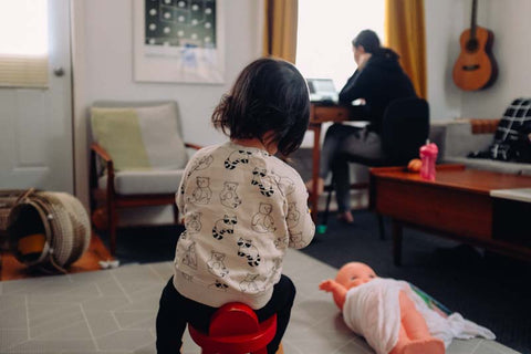 woman in background on laptop and child playing in same room