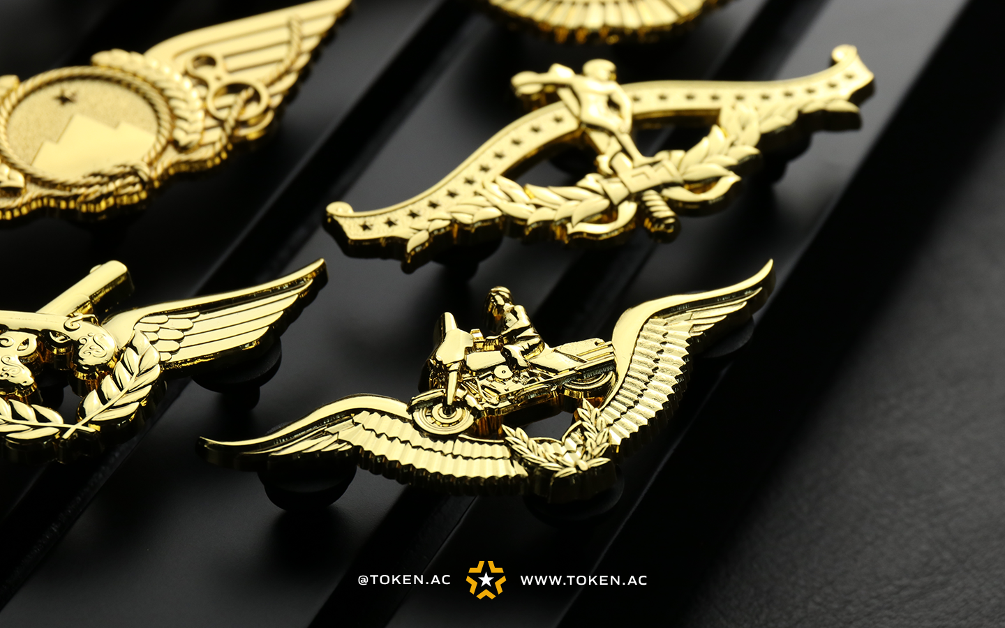 Diversos tipos de brevês e distintivos militares, dourados e prateados, expostos sobre um fundo escuro.