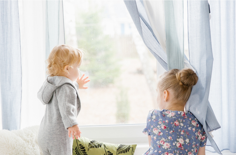 ID: Two small children sitting on a couch looking at the window