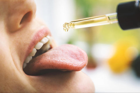 Pipette, die Vollspektrum CBD-Öl in Bioqualität in den geöffneten Mund einer Frau tropft
