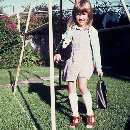 rini on her first day of school, holding a toy dog, a satchel, and sitting on a swing set