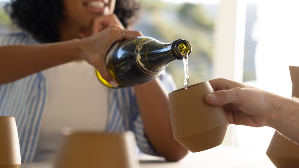 A group of friends sit around a table drinking champagne out of ceramic wineware