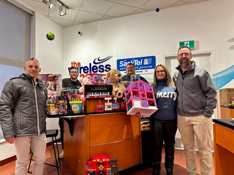 A group of people, from the Wireless Age and Custom Courier stand in front of toys for donation.