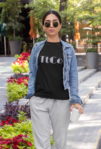 woman walking holding a coffee cup wearing a tiredteacherco black signature soft t-shirt with silver TtCo logo, a fashionable blue jean jacket and comfortable soft cotton sweatpants.