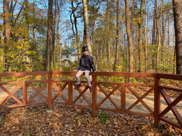 Girl sitting on a wooden fence by a forest path